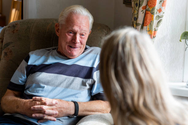 Having a Chat with a Patient Nurse conversing with a senior patient in the North East of England while he is sitting in a chair in his living room. alzheimer patient stock pictures, royalty-free photos & images