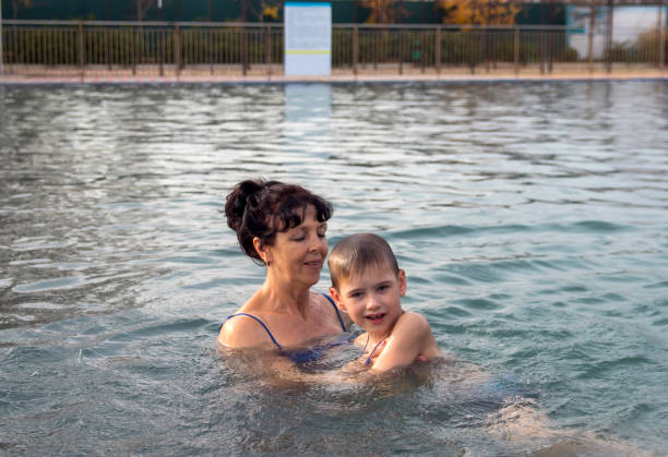 oma und enkel spielen und schwimmen im herbst in einem pool mit warmem wasser. - active seniors retirement enjoyment swimming pool stock-fotos und bilder