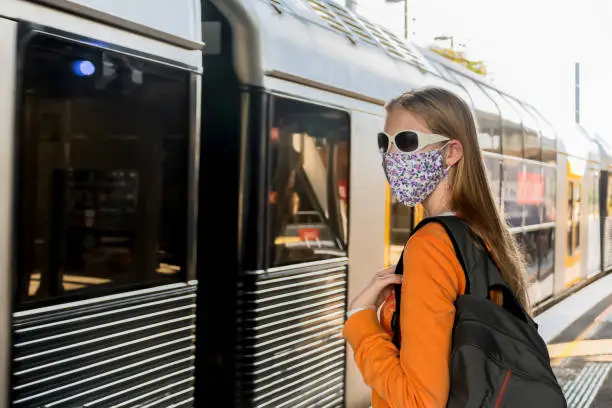 Photo of Teenage girl wearing face mask waiting for the train on the platform. Sydney trains transport NSW during Covid-19 pandemic. Mandatory face masks in public transport