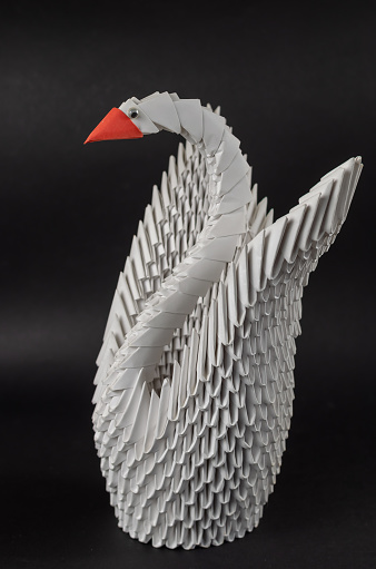 Japanese modular origami. White paper swan against a black background. Creativity skill art hobby. Selective focus
