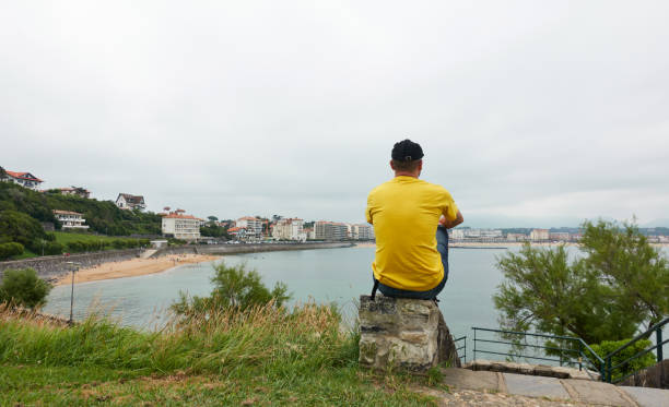 istock thoughtful man sitting on a small wall looking at the beach on a cloudy summer day 1355259466