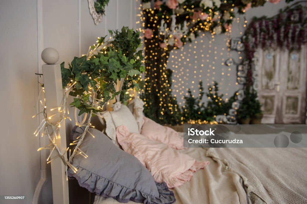vintage photo zone: a white bed and a decorative tree decorated with plants and light bulbs lateral view of a vintage photo zone: a white bed and a decorative tree decorated with plants and light bulbs Flower Stock Photo