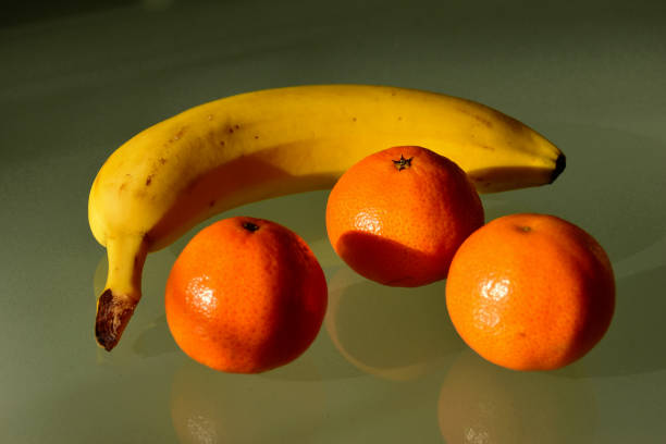 yellow banana and orange color clementines groupped. close-up view on reflective glass - groupped imagens e fotografias de stock