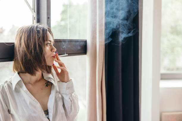 istock Young woman smoking a cigarette in hotel room. 1355260978