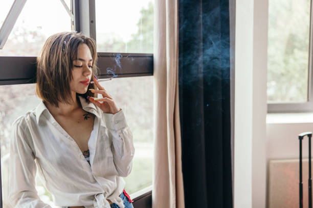 istock Young woman smoking a cigarette in hotel room. 1355261165