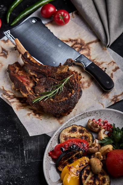 istock Tomahawk steak with vegetables and a knife on the table. Grilled meat with grilled vegetables and fresh vegetables on the table 1355265343