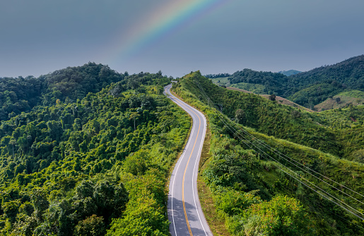 Aerial view of  road through the green forest and texture background as highway of empty and Rainbow road after storm rain