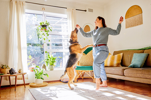 Full length shot of an attractive young woman dancing with her dog in the living room at home