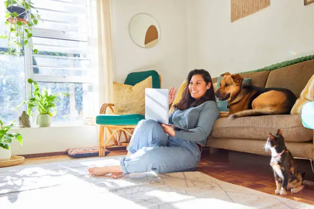 Photo of Full length shot of an attractive young woman sitting in her living room with her pets and using her laptop