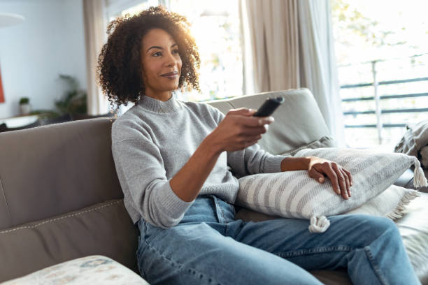 istock Relaxed mature woman changing channels with the remote control while watching TV on the sofa at home. 1355275764