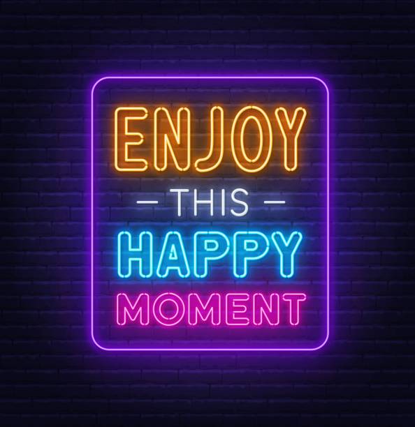 istock Enjoy This Happy Moment neon quote on a brick wall. 1355275915