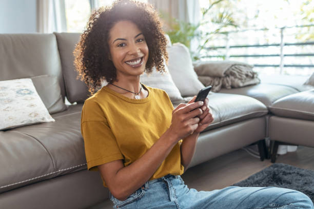 istock Happy mature woman using smartphone while relaxing sitting on the floor looking at camera at home. 1355276741