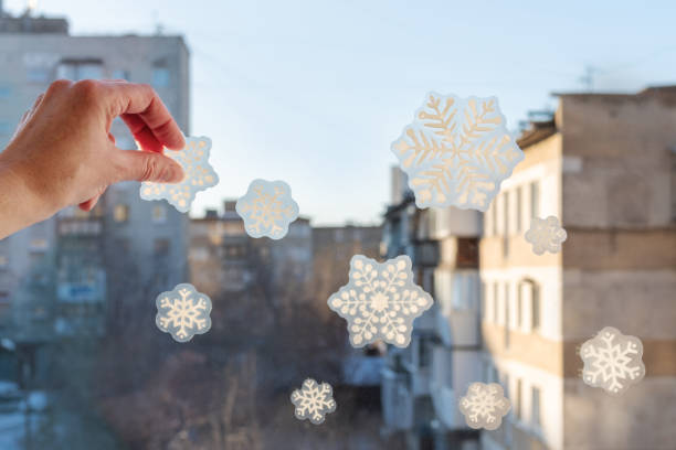 Hand pasting hand-made snowflake stickers on the window of a house. Snowflake pattern on window glass.