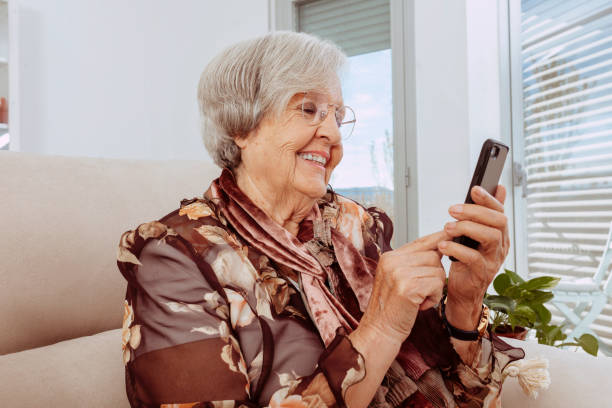 istock Old grandmother using smartphone sitting on couch at home 1355287930