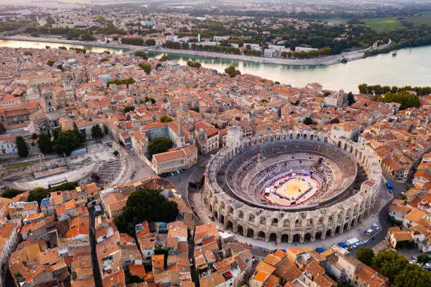 Aerial view of Arles townscape on bank of Rhone river overlooking restored antique Roman amphitheatre and ruins of Gallo-Roman theatre on autumn day, France