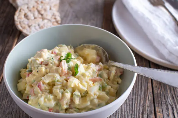 Healthy high protein egg salad made with low fat mayonnaise, yogurt, and vegetables such as onions, chives, bell peppers and celery. Served in a bowl with spoon on a wooden table