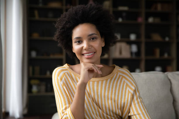 Happy millennial African American girl home head shot portrait Happy millennial African American girl home head shot portrait. Smiling young woman looking at camera, talking on video call, sitting on couch, speaking online, touching face. Screen view divergent movie review stock pictures, royalty-free photos & images