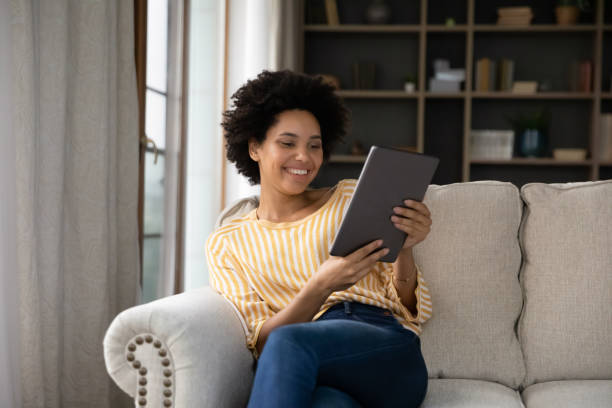 istock Happy young Black girl relaxing on sofa, using tablet computer 1355293332