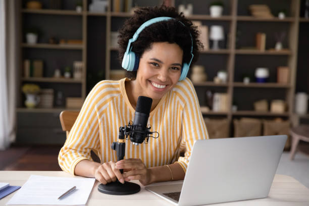 Happy young Black woman in headphones and professional microphone recording Happy cheerful young Black woman in headphones and professional microphone recording audio podcast for radio, live channel on internet, presenting news on air. Newscaster, blogger head shot portrait television host stock pictures, royalty-free photos & images