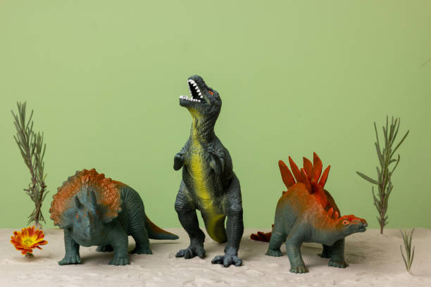 istock Toy dinosaurs stand on the sand on a green background. 1355294857
