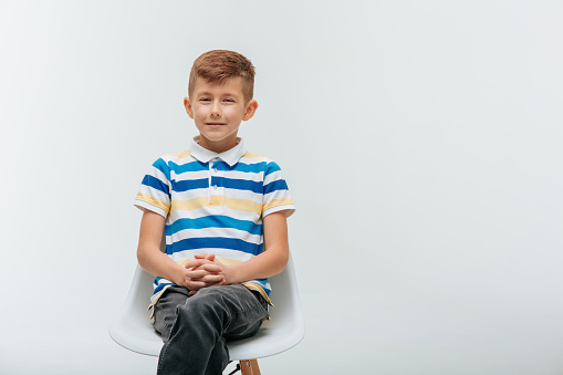 kid boy sitting on chair in studio and looking at camera. nice child in t-shirt with colored lines