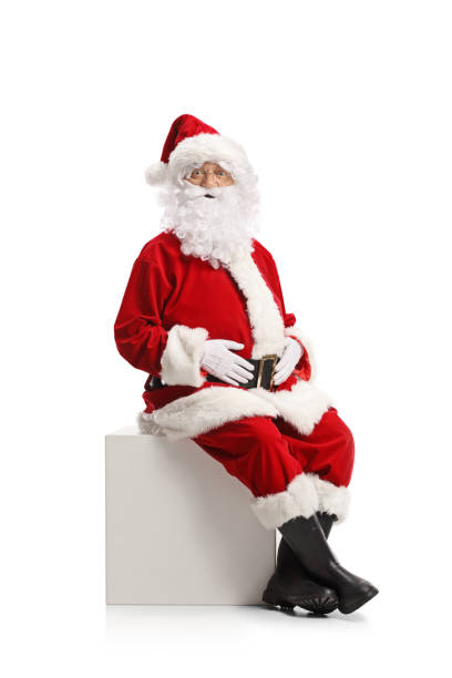 istock Santa claus sitting on a white cube and looking at camera 1355295951