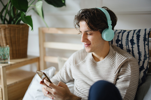 Young man using dating app on his smartphone while listening to music on wireless headphones