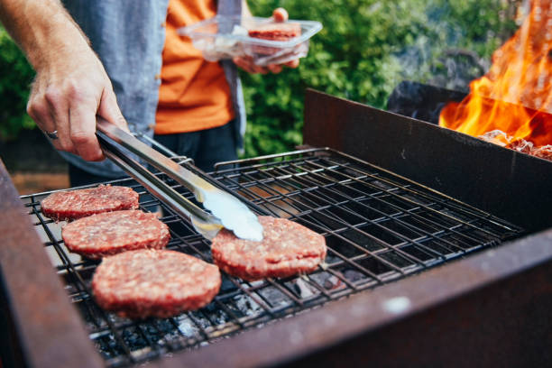 foto de un hombre asando hamburguesas durante una barbacoa - barbacoa fotografías e imágenes de stock