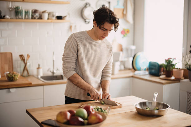Young man preparing lunch in the kitchen, cutting Brussels sprout into tiny pieces