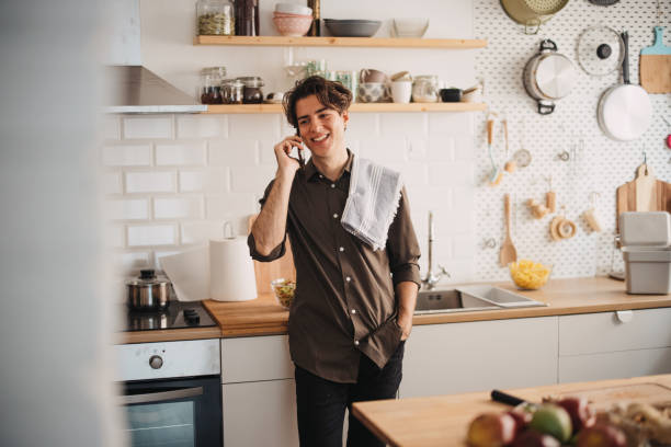istock Young man smiling and talking on the phone in kitchen 1355297332