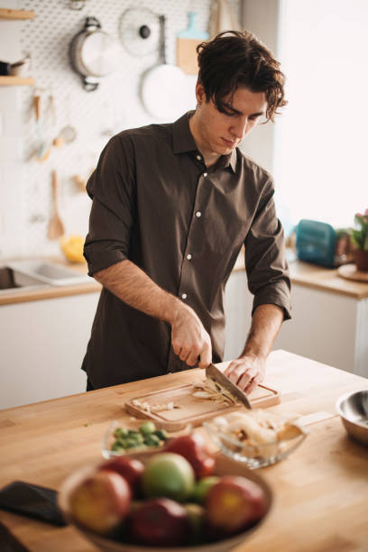 istock Young man preparing lunch in the kitchen, cutting Brussels sprout into tiny pieces 1355297335