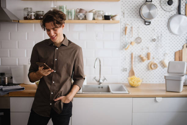 giovane che sorride e parla al telefono in cucina - mescolare foto e immagini stock