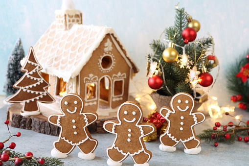 Christmas house made from gingerbread. Playfully decorated with colourful gummy bears. Christmas tree in background with lights. Festive New year atmosphere and mood.