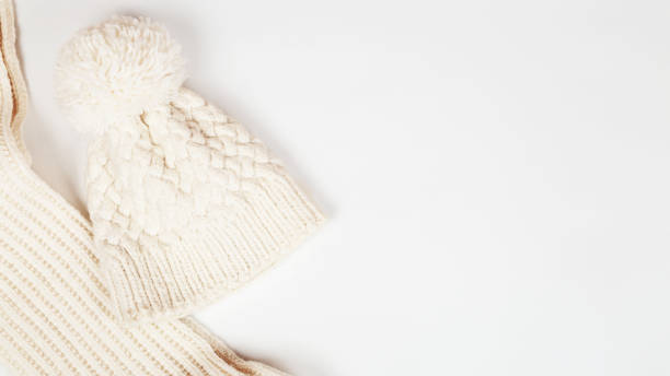 istock Knitted scarf a pipe or collar from warm threads and a white cap with a pom pom. Accessories for autumn and winter. Copy space, top view, flat lay 1355300365