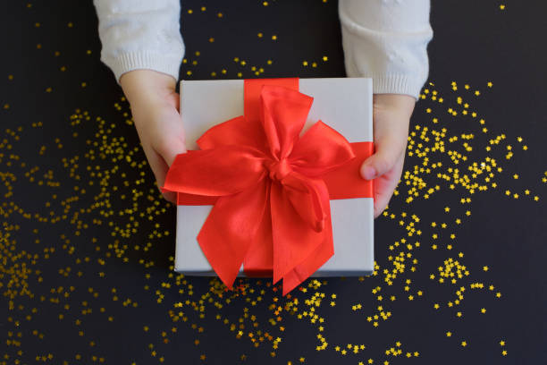 istock Baby hands holding present with red bow on fastive background with gold sparkles. 1355301378