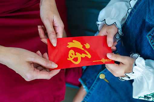 Young Asian Chinese girl receiving red envelope from her mother in Chinese New Year.