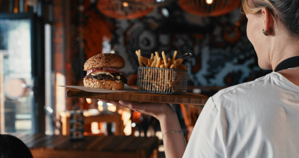 tiro de uma garçonete servindo um hambúrguer com batatas fritas em um restaurante - restaurant waiter food serving - fotografias e filmes do acervo