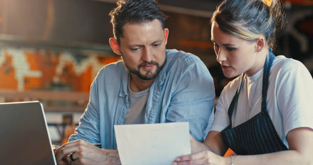 istock Shot of a young man and woman using a laptop and going over paperwork while working in a restaurant 1355304517