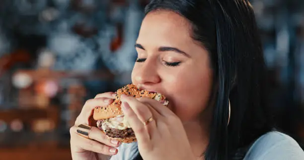 Photo of Shot of a young woman enjoying a delicious burger at a restaurant