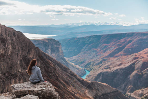 Girl sits and admires the picturesque view of the beautiful canyon. Girl with long brown hair sits and admires the picturesque view of the beautiful canyon. Backside view. Mountain azure river. north caucasus photos stock pictures, royalty-free photos & images