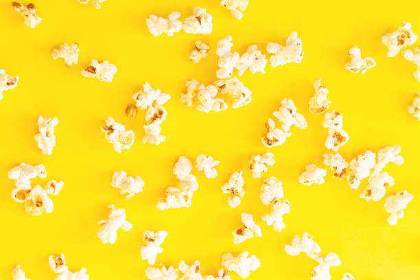 istock Scattered cinema popcorn on yellow background overhead 1355315190