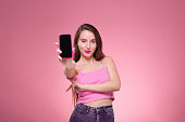 Beautiful young adult caucasian holding a smart phone in an all pink theme studio portrait