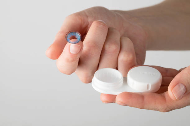 istock A woman's hand with a colored contact lens on her finger and a container on a light background. 1355329285