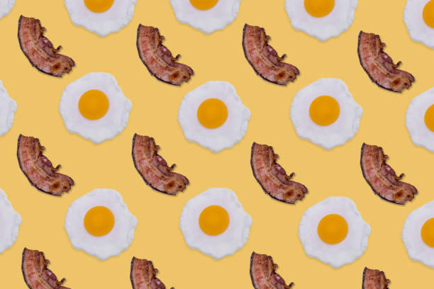 istock Creative food Pattern made with fried eggs and slices of crispy bacon on bright yellow background. 1355333240
