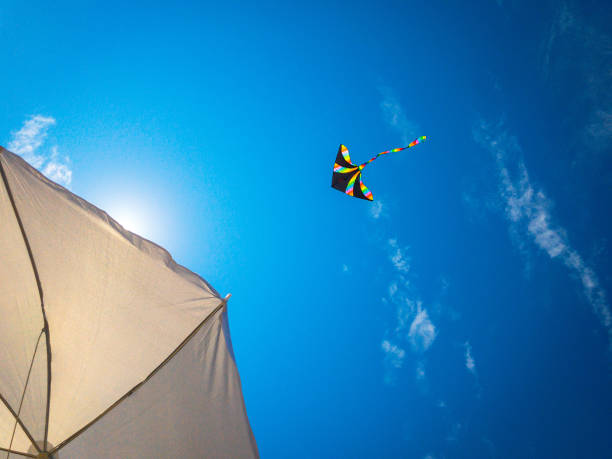 istock Kite clouds. Colorful high flying toy. Air kite fly on blue wind sky background with copy space. Rainbow summer kite. Festive, happiness, success background. 1355334281