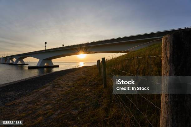 Zeeland Bridge In Netherlands Construction Of Concrete And Steel Connects The Municipalities Of Schouwenduiveland And Noordbevelandpasture Fence In The Foreground In The Evening Before Sunset Stock Photo - Download Image Now