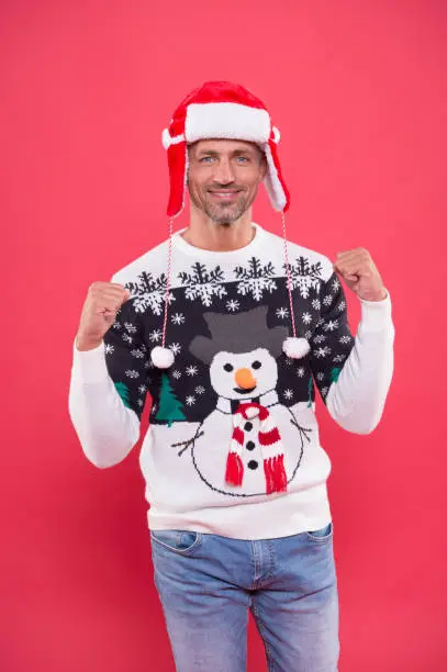 unshaven man funny sweater red background. male cold weather fashion. santa man ready for winter holiday. xmas party and activity. christmas is here. happy new year. sexy man santa earflap hat.
