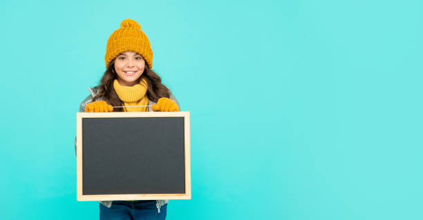 istock happy kid in hat hold school blackboard with copy space on blue background, announcement 1355336099