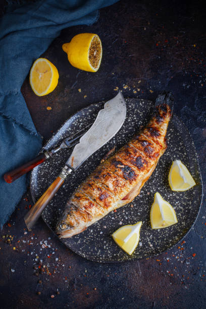 레몬과 조미료, 칼이 있는 구운 송어를 접시 근처에 얹습니다. - trout prepared fish whole grilled 뉴스 사진 이미지