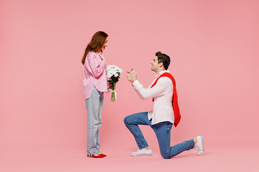 Full body side view young couple two friends woman man 20s in shirt making proposal give ring isolated on plain pastel pink background studio Valentine's Day birthday holiday party engagement concept